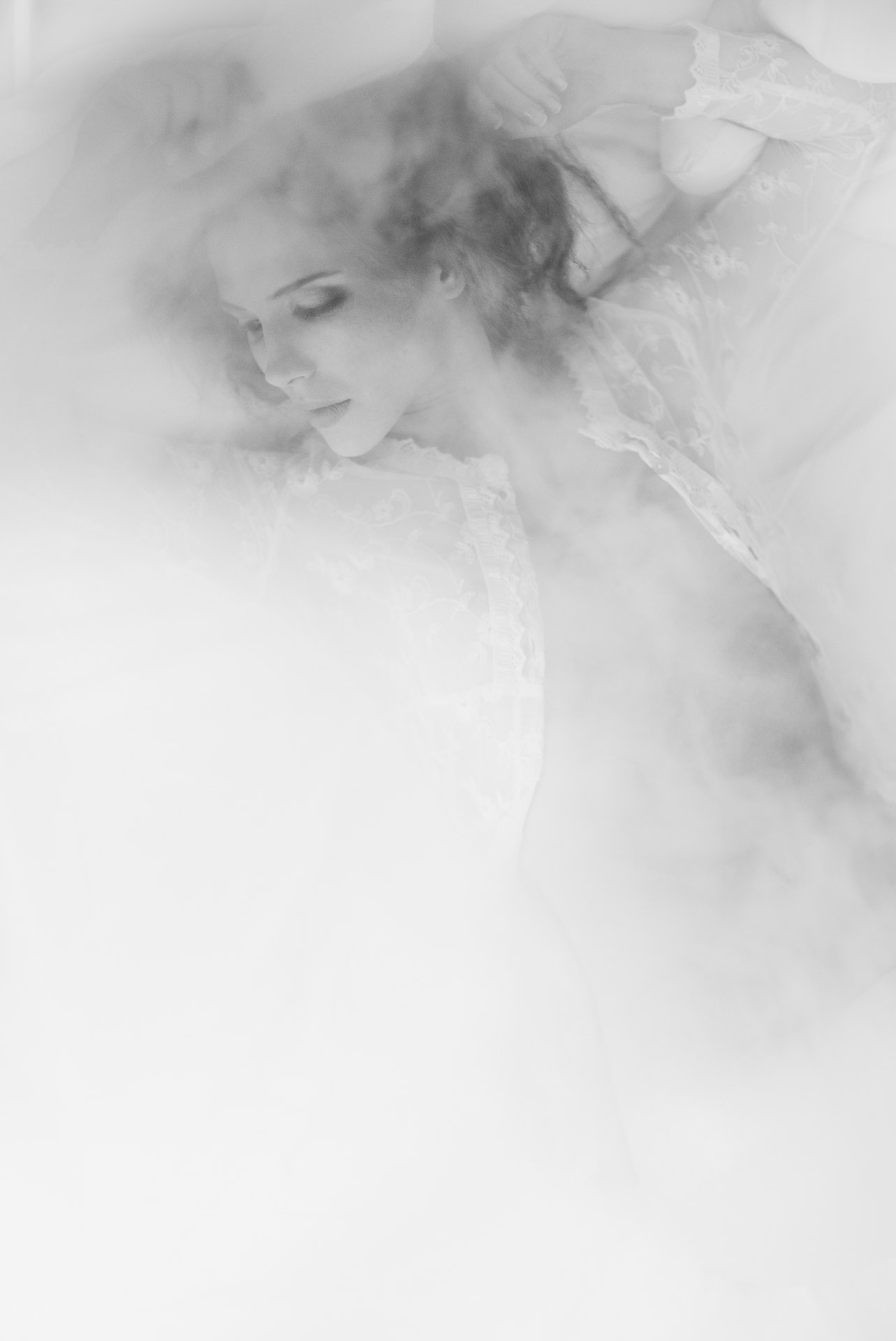 Woman with arms raised behind head in profile, soft-focus portrait dissolving into white background with romantic vignette effect