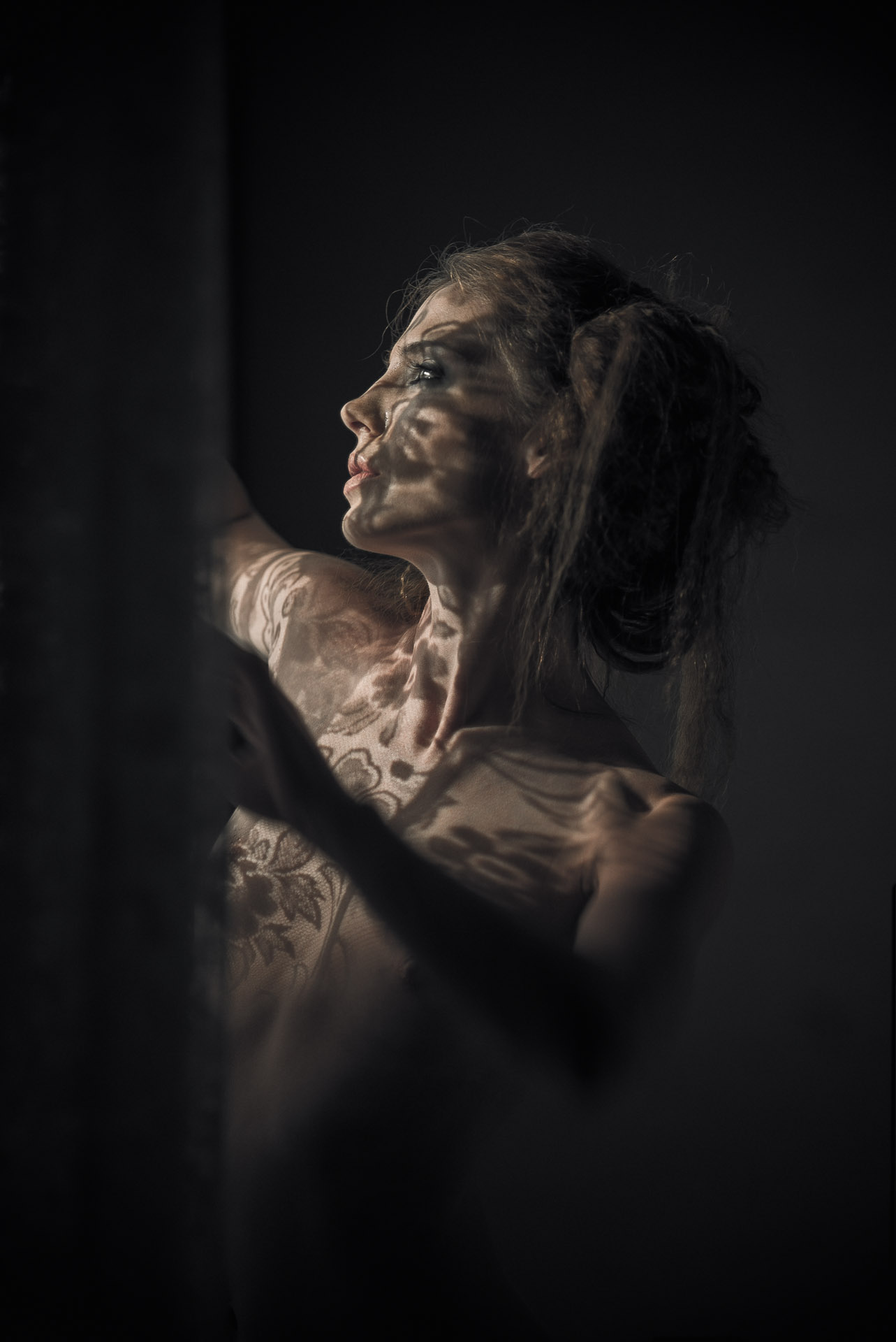 Woman in profile looking upward with dramatic side lighting highlighting her face and shoulder against black background